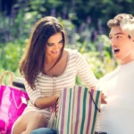 Młody facet i uśmiechnięta dziewczyna na ławce w parku obok toreb z zakupami