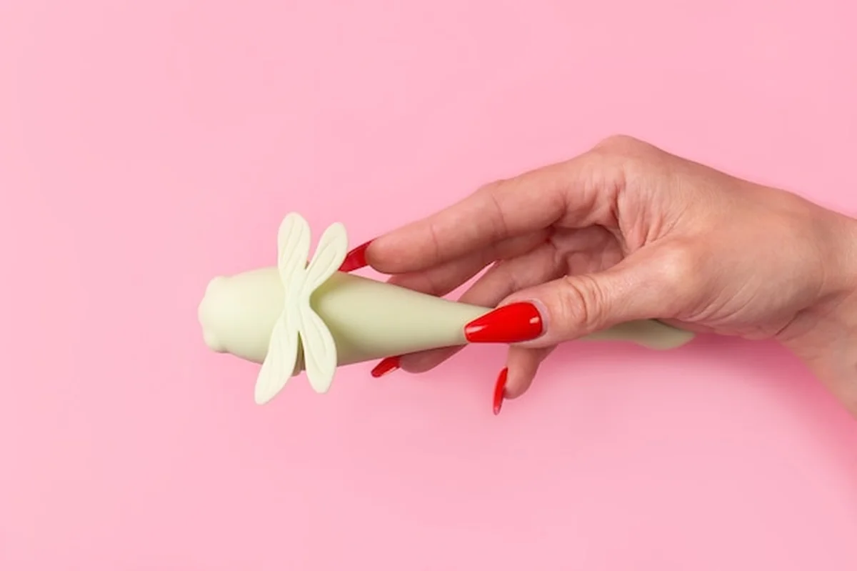 Dildo w dłoni na różowej ścianie