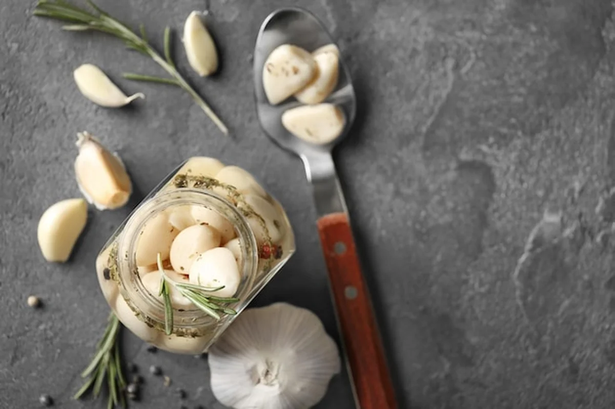 Konserwowany czosnek w szklanym słoiku na szarym tle