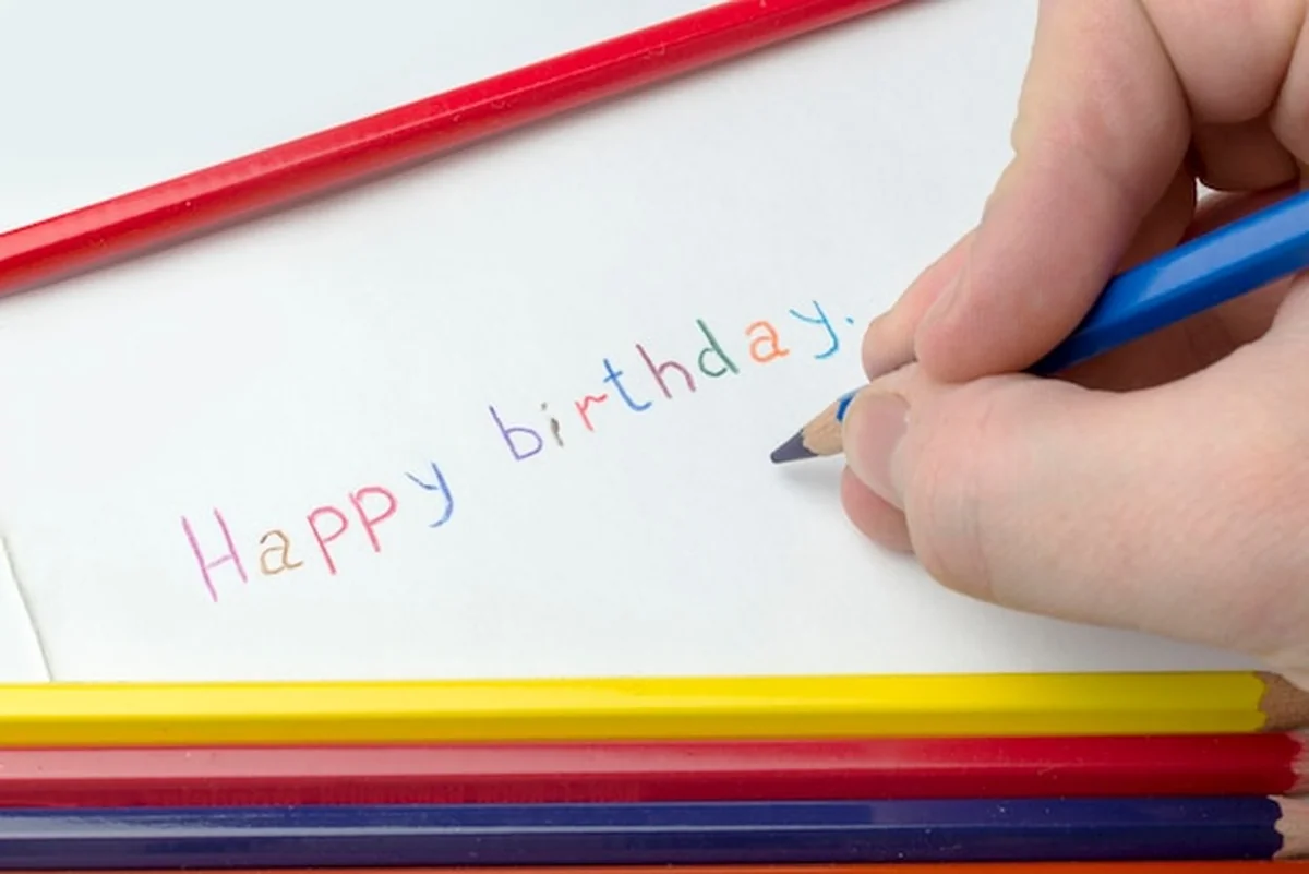 Ręka z ołówkiem pisze życzenia urodzinowe na papierze