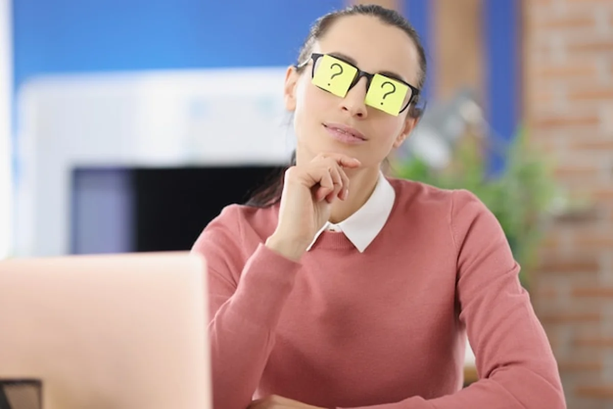 Młoda kobieta z naklejkami ze znakiem zapytania na okularach w biurze