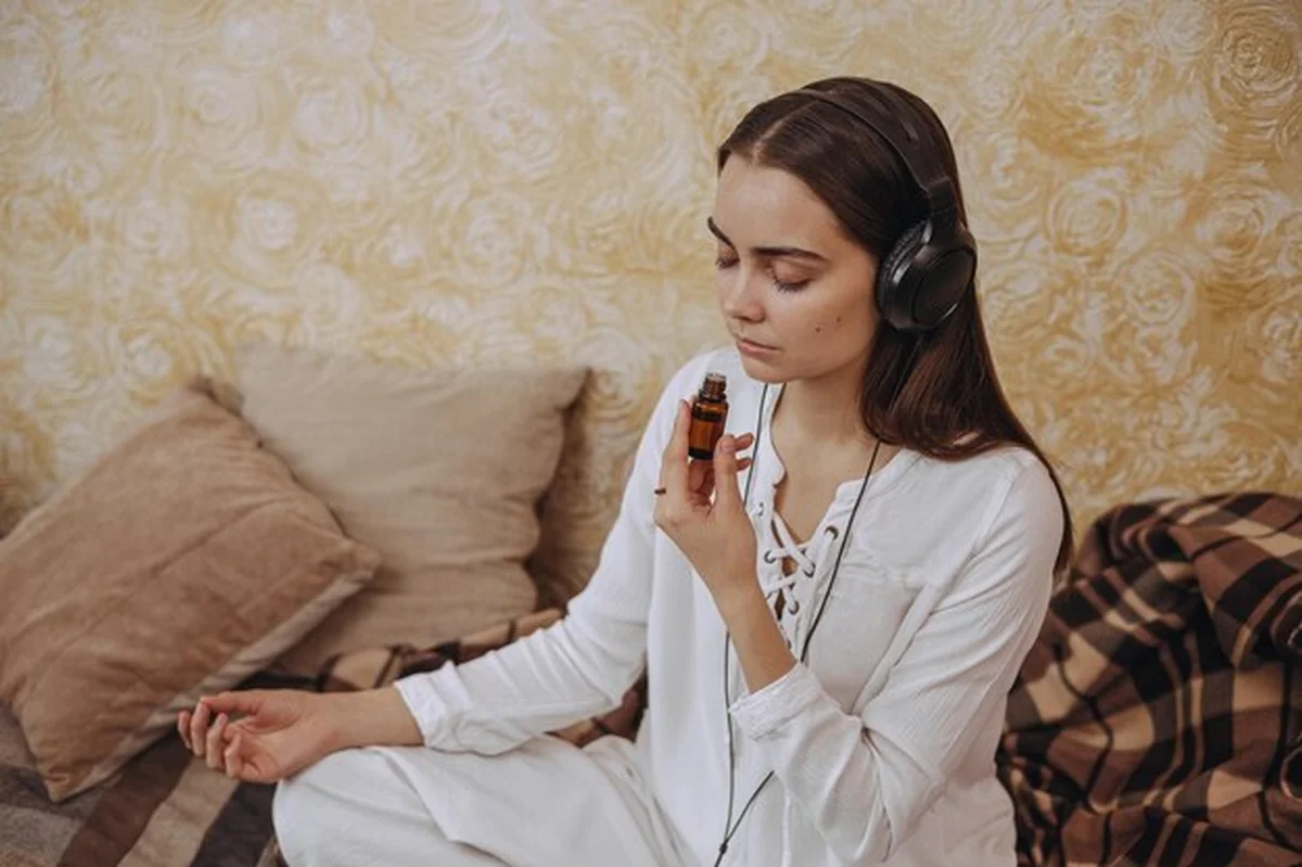 Kobieta słuchająca medytacji w słuchawkach i wąchająca olej eteryczny podczas aromaterapii w domu