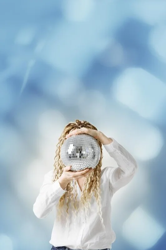 Kobieta trzymająca kulę dyskotekową przed twarzą na tle niebieskiego rozmytego bokeh - kreatywna celebracja