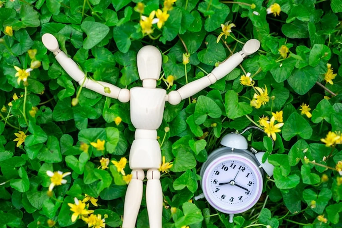 Mężczyzna odpoczywa na zielonych liściach z budzikiem