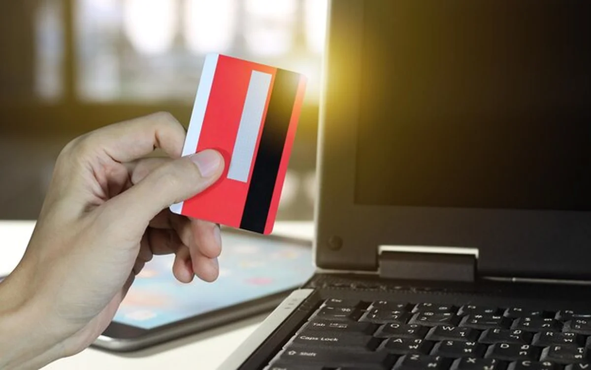 Ręka trzymająca kartę kredytową przez laptop na stole